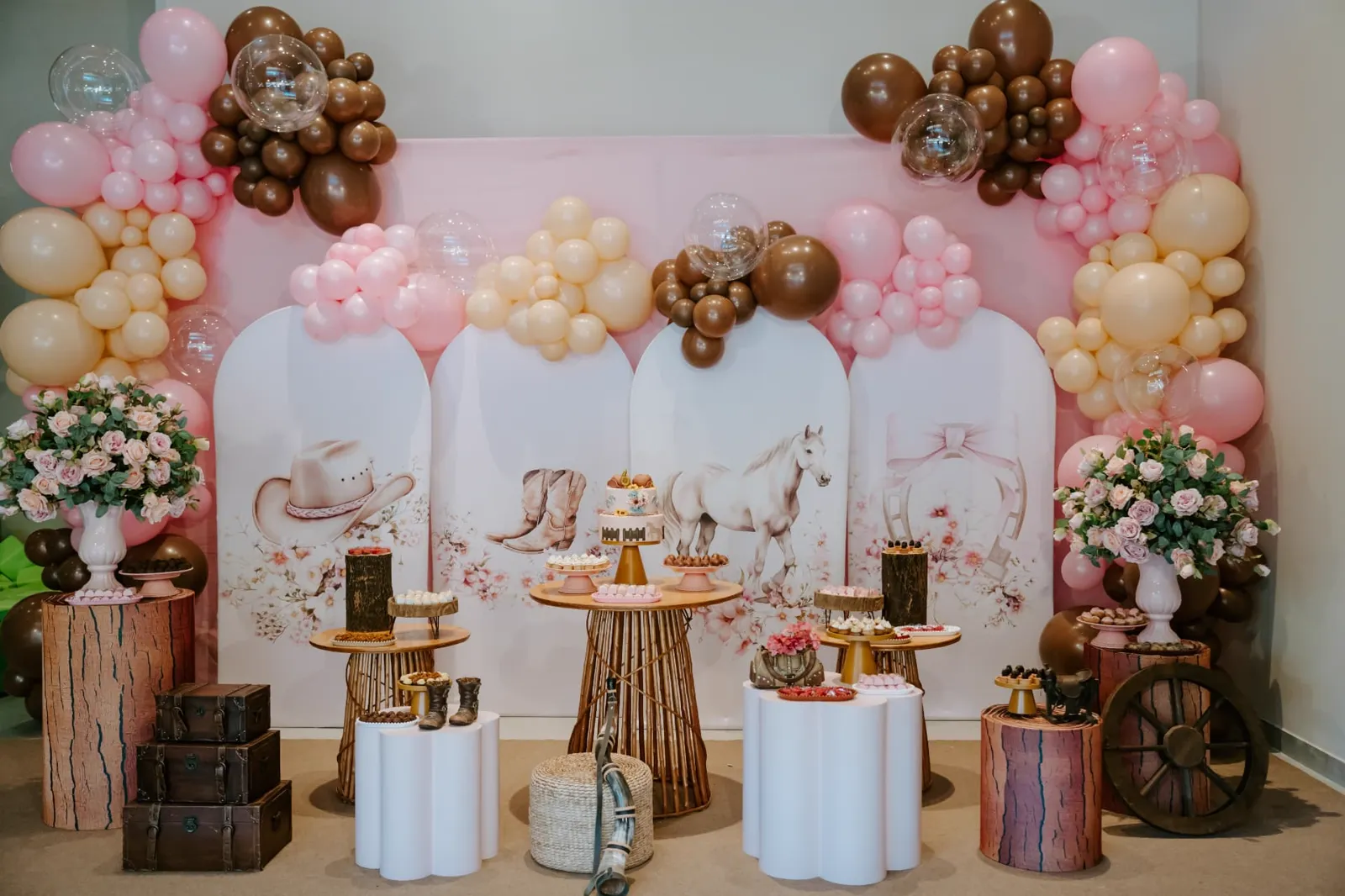 Decoração de festa com tema vaqueira: painéis ilustrados, arcos de balões em tons de rosa e nude, bolo e docinhos