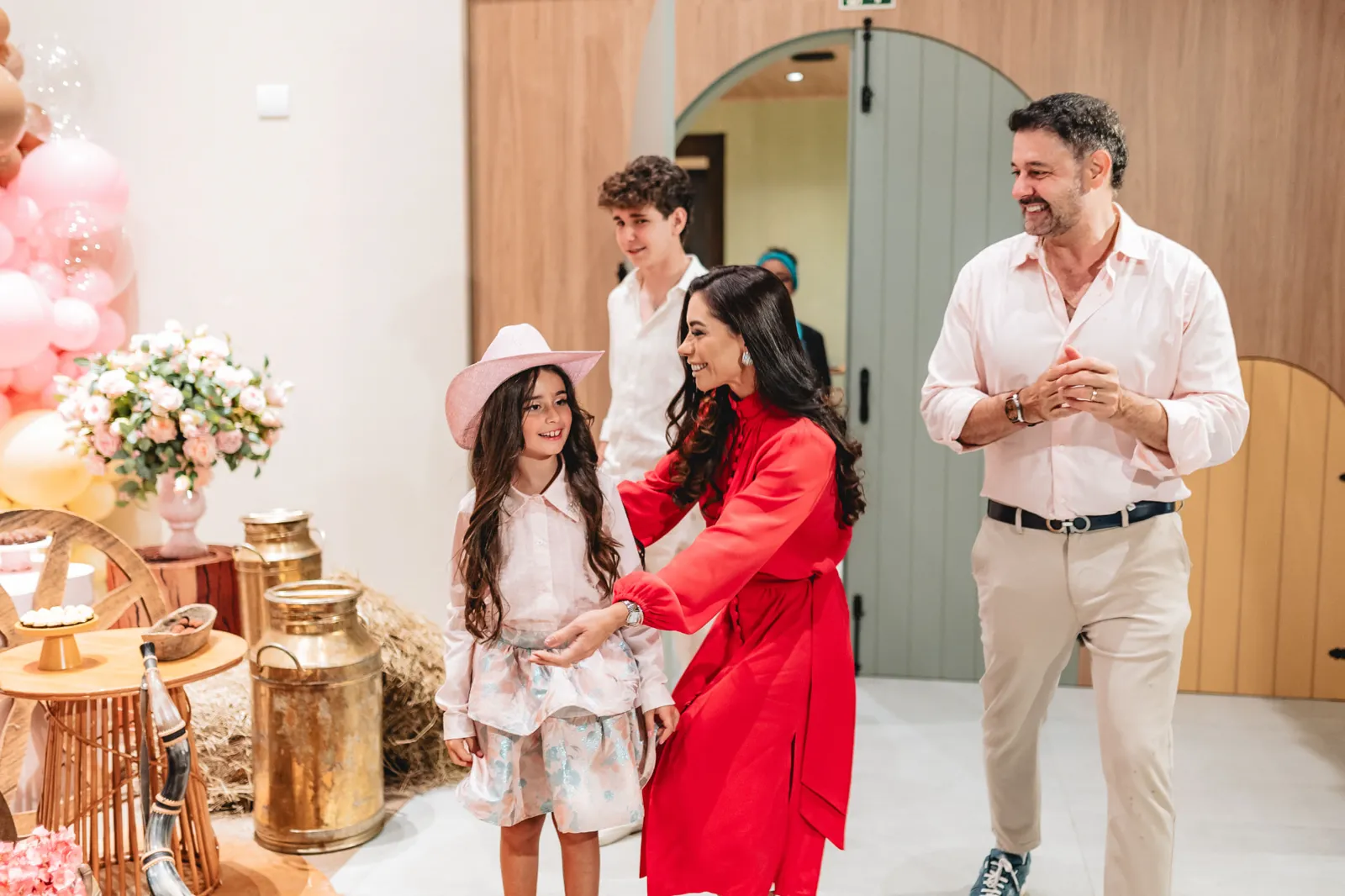 Família na chegada à festa, junto à decoração, com menina de chapéu rosa