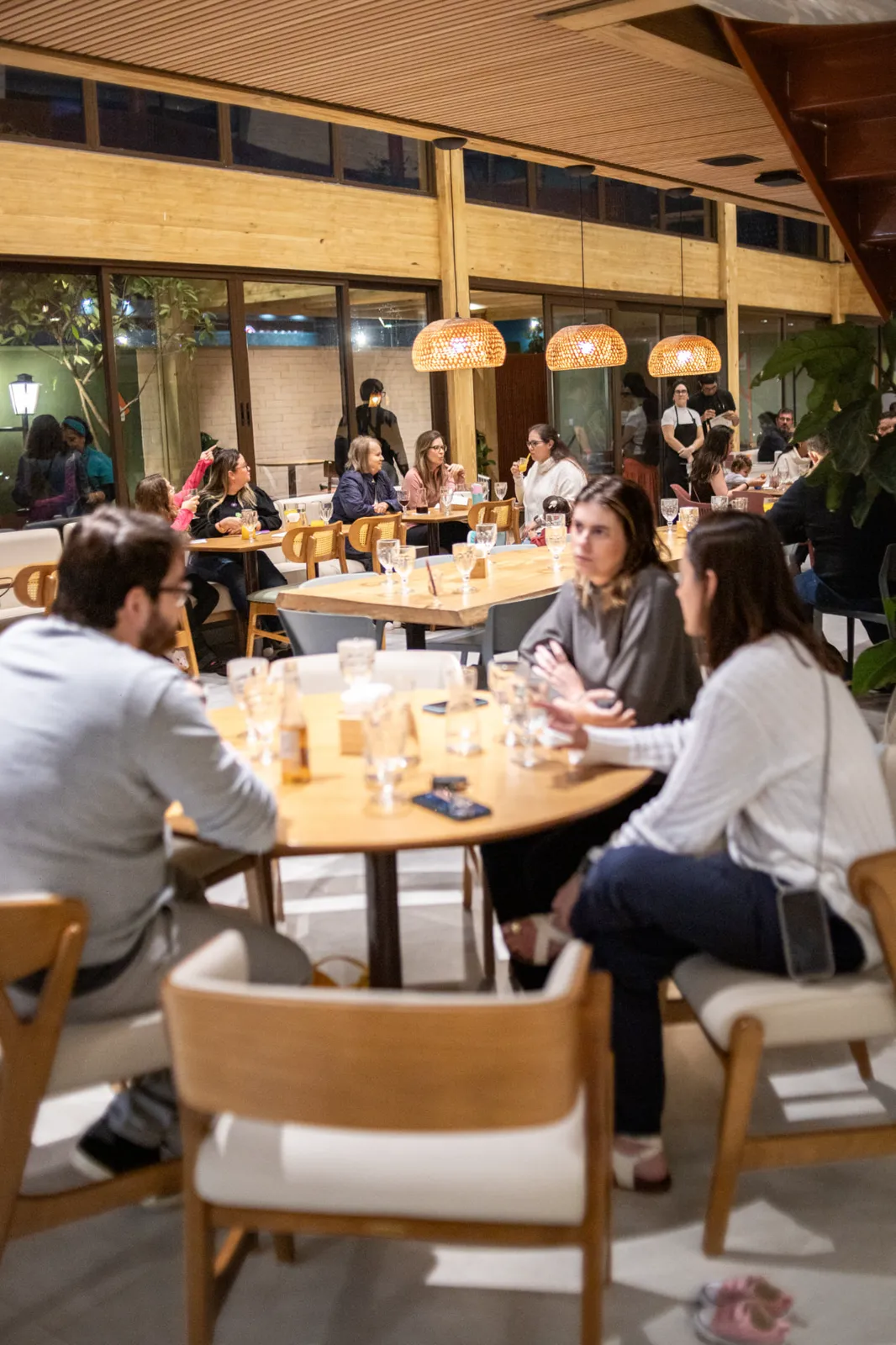 Salão de refeições à noite com mesas de madeira e vista para o jardim