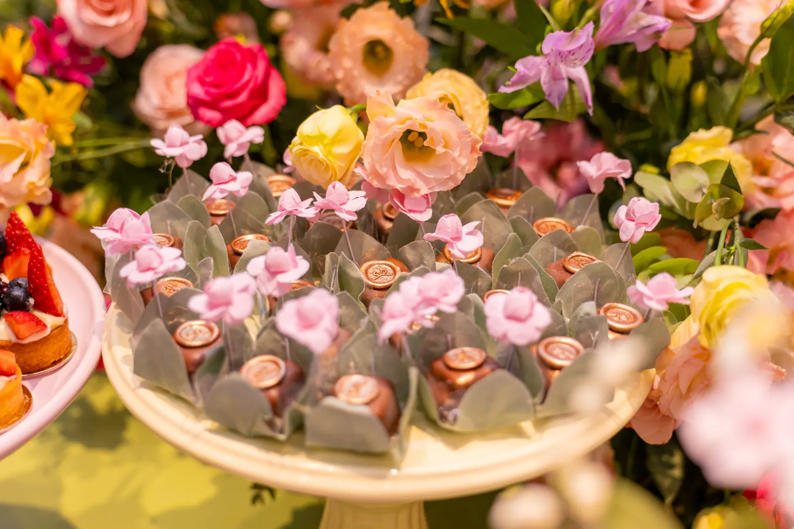 Mesa de doces finos com bombons, minitortas de frutas e arranjo floral