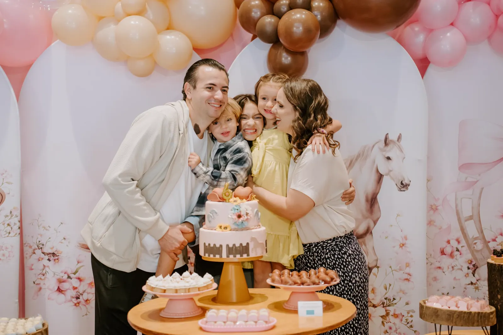 Família com três filhos posando atrás da mesa de doces e do bolo